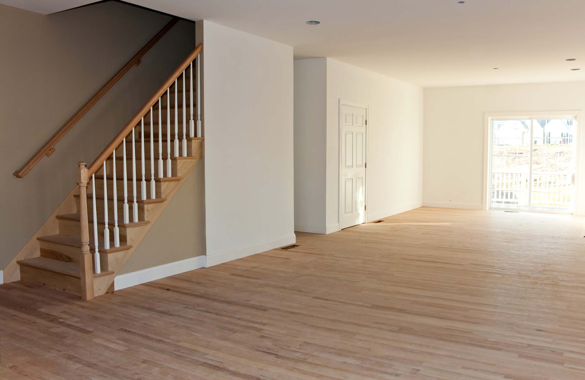 Newly Built House Interior. New home construction interior room with unfinished wood floors stairway and railings. Electrical and hvac connections also are partially unfinished.